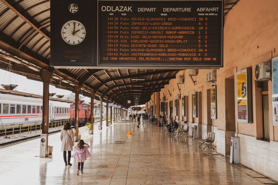 Peron üzerinde yolcular otobüs ve trenlerin zaman çizelgesini incelemek için bekliyor